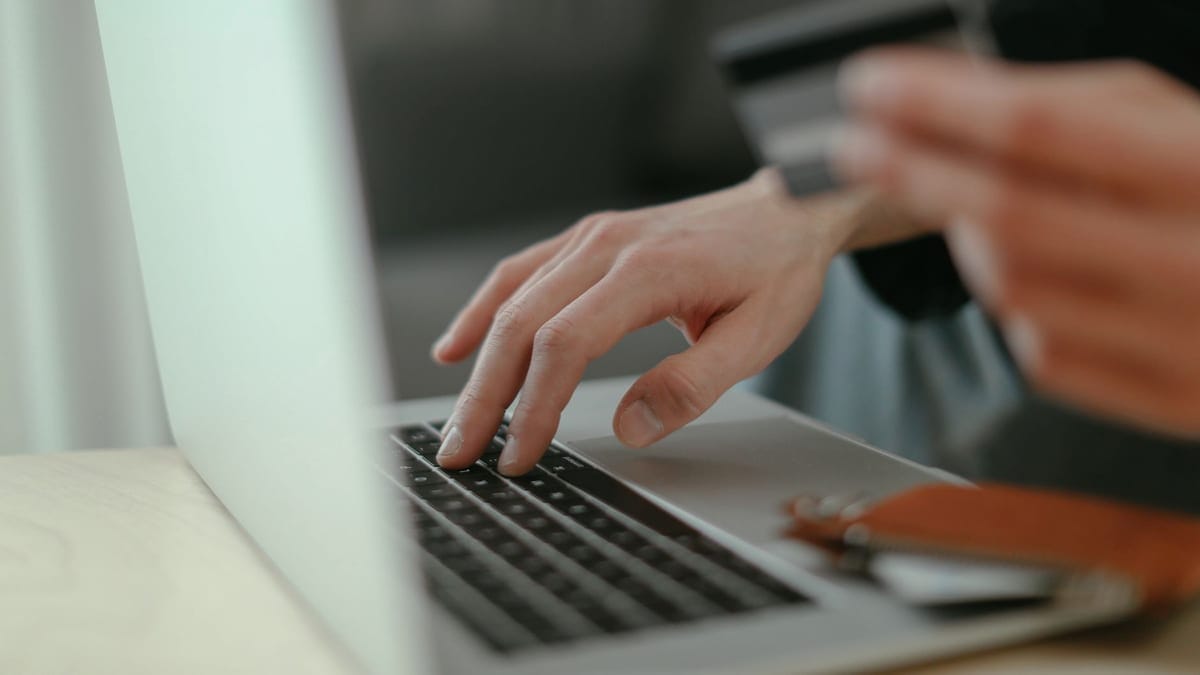 Close-up of hands holding a credit card and typing on a laptop keyboard for online shopping.