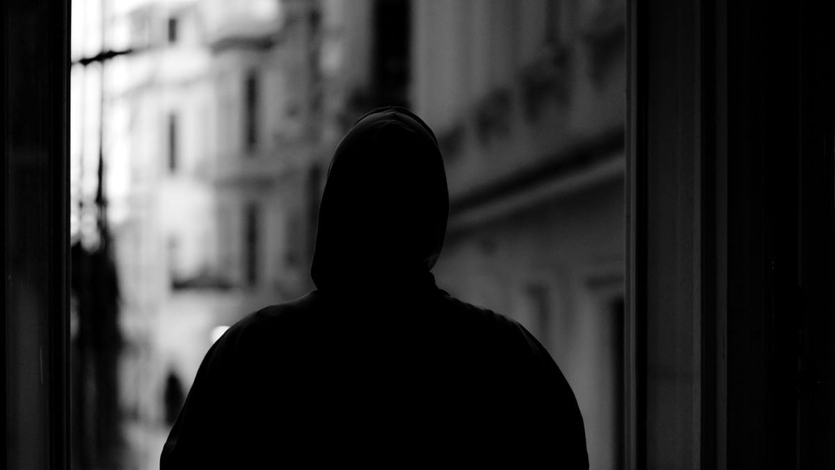 Black and white image of a hooded figure in an urban environment, creating a mysterious silhouette.