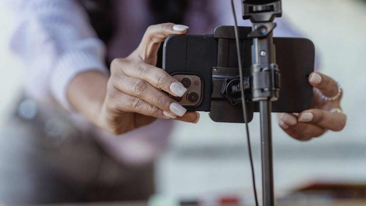 Crop unrecognizable female setting mobile phone on tripod while recording vlog on blurred background