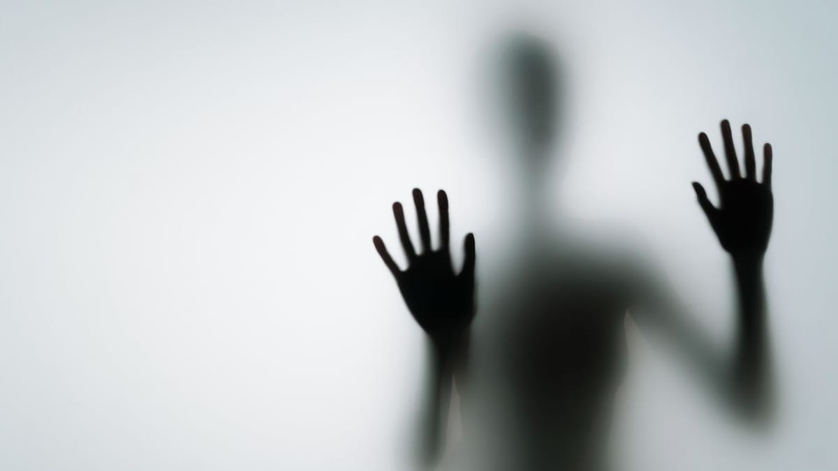 Abstract silhouette of person with hands against glass, creating a mysterious vibe.