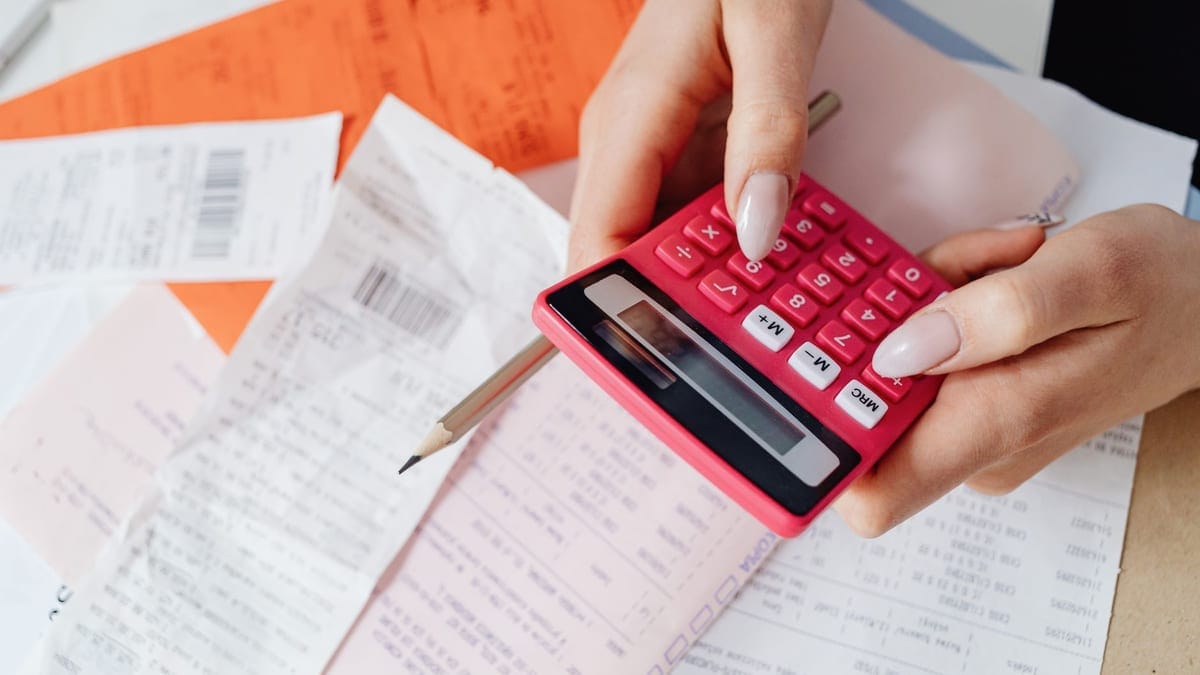 Hands using a pink calculator to manage expenses amidst various receipts and documents.