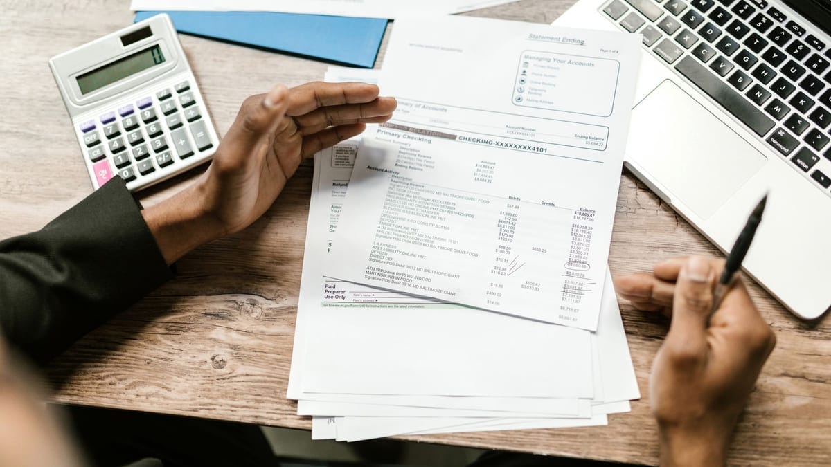 Hands holding financial documents with calculator and laptop on office desk, business analysis scene.