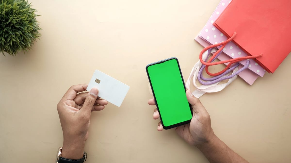 Top view of hands holding a smartphone and credit card for online shopping on a beige background.