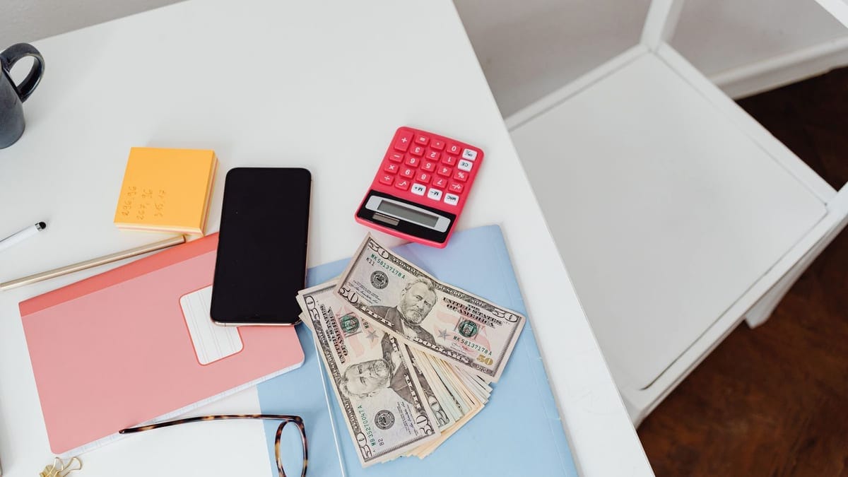 Overhead view of office desk with calculator, money, and glasses, depicting finance and budgeting.