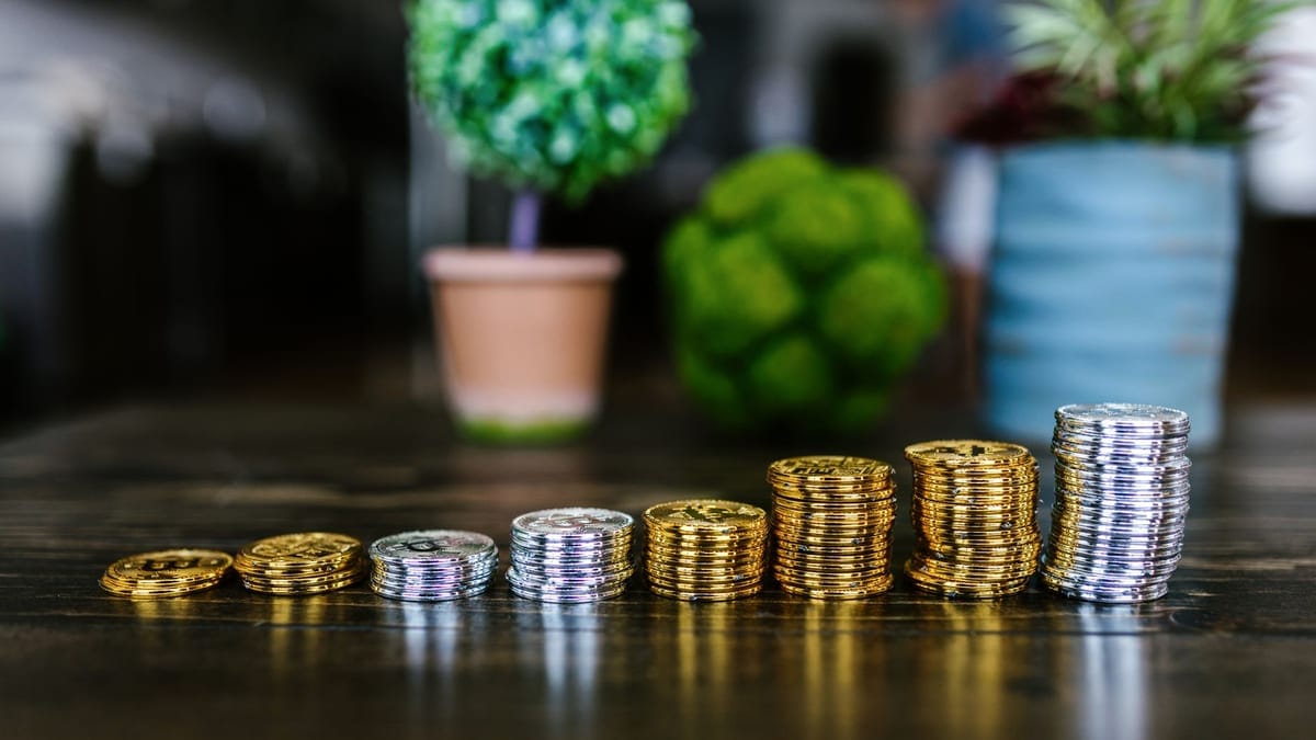 Close-up of stacked gold and silver bitcoins on a wooden table with plants in the background.
