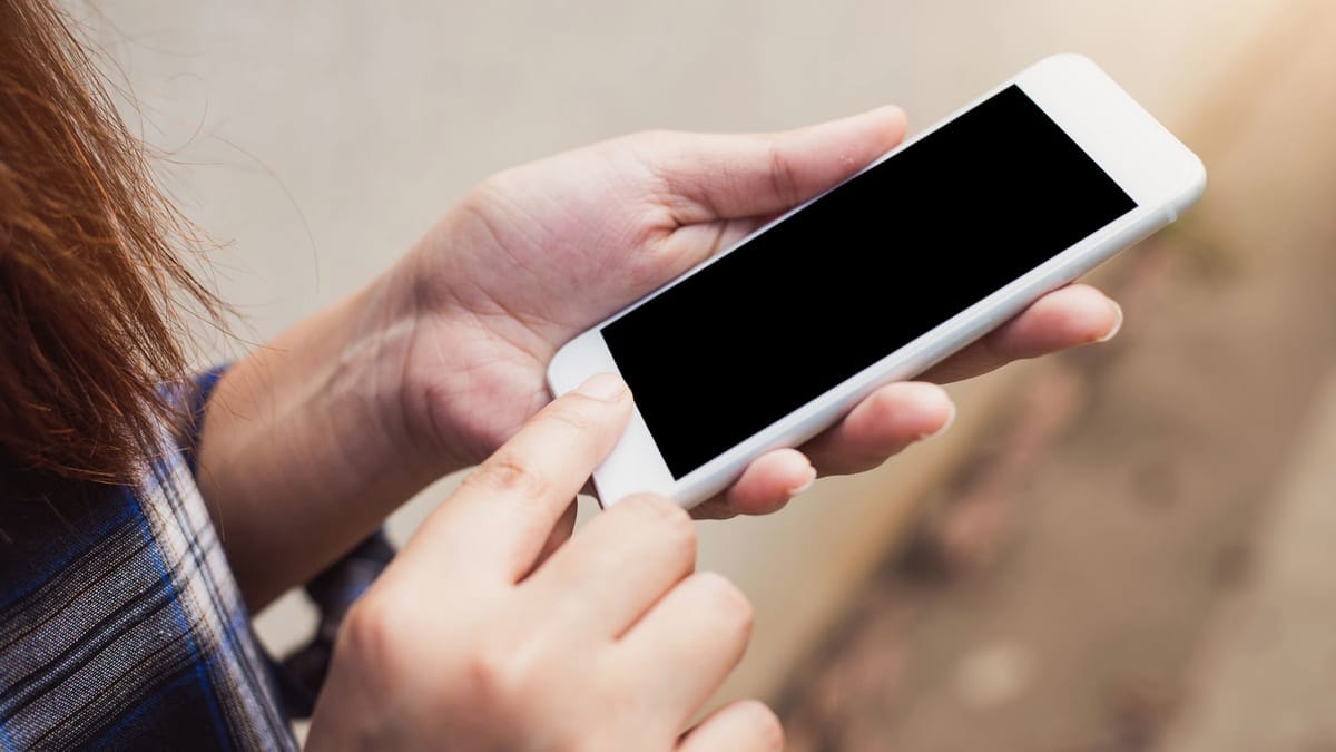 Person holding and using a smartphone outdoors, focusing on hands and screen.