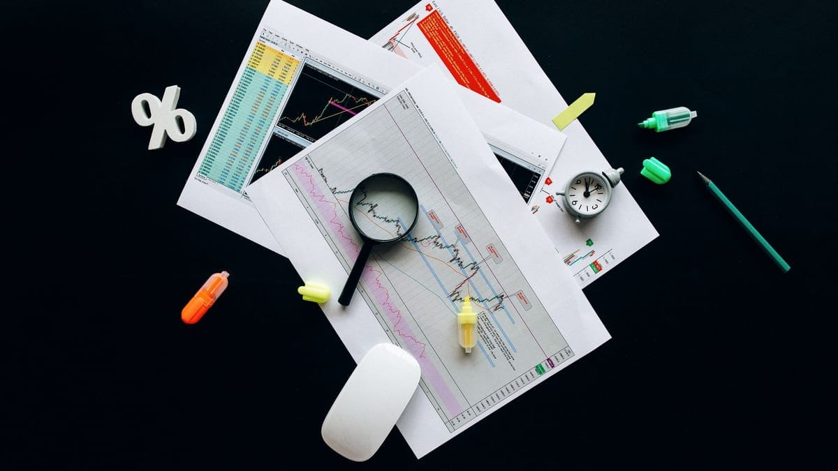 Overhead view of an office desk with financial documents, a magnifying glass, and stationery items, suggesting business analysis.