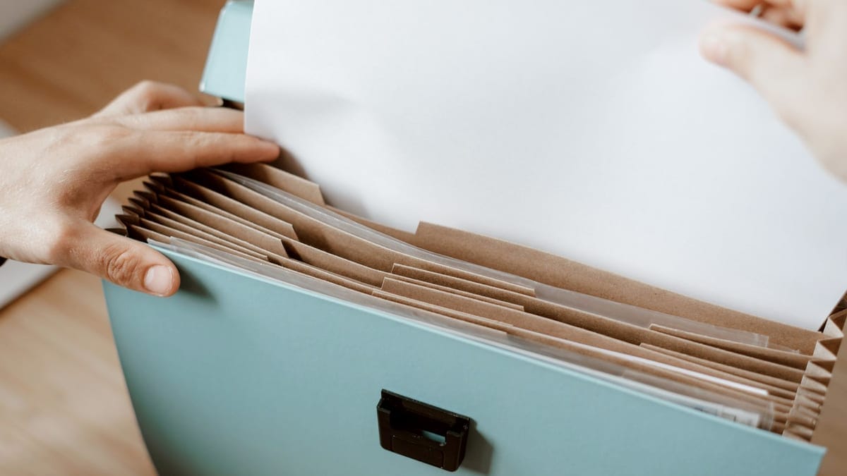 Crop faceless person putting sheet of paper in briefcase for documents placed on table