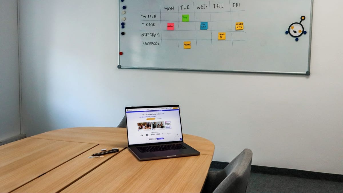 Office setup featuring a conference table, laptop, and organized whiteboard schedule, highlighting a tech-driven workspace.