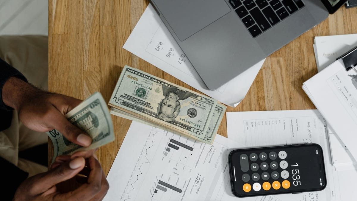 Close-up of hands counting cash on desk with calculator, charts, and laptop, illustrating financial management.