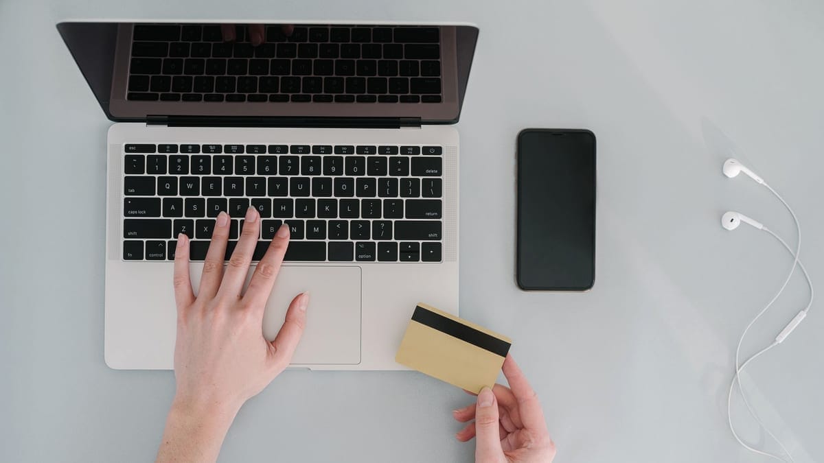 Flat lay of a workspace with a laptop, bank card, smartphone, and earphones, ideal for online finance themes.